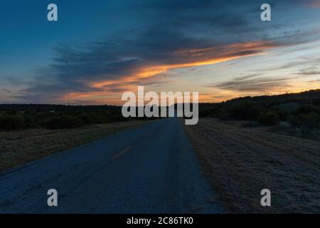 A beautiful band of gray clouds with the side facing the setting sun glowing orange and yellow as the sun sets behind some trees in the distance down Stock Photo
