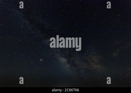 Heart of the Milky Way in a night sky full of stars with some light, wispy clouds passing by overhead. Stock Photo