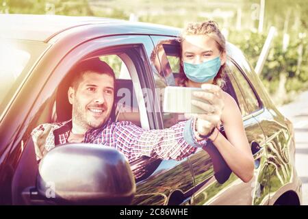 Happy couple wearing face masks having fun taking selfie during local traveling at countryside Stock Photo