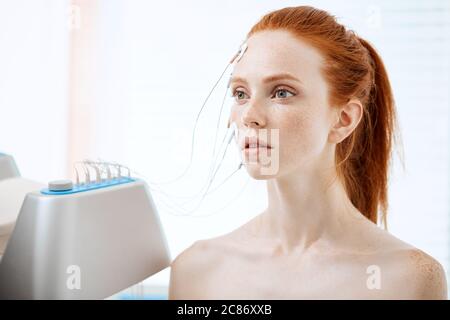 Young woman lying with electrodes on her face, receiving electric stimulation on skin. Professional equipment for microcurrent lift face. Anti aging f Stock Photo