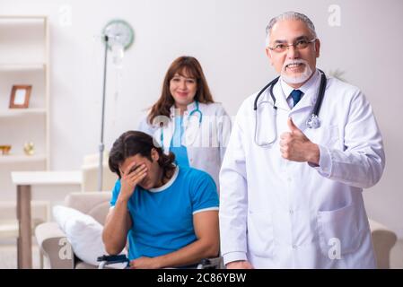 Two doctors visiting sick man at home Stock Photo