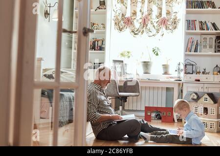 Mature man looking photo book and his grandson using digital tablet Stock Photo