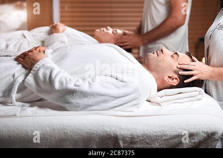 Handsome caucasian businessman and his beautiful wife treating themselves to a comforting back massage, a gentle relaxing massage at spa clinic. Stock Photo