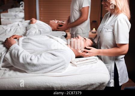 Close up shot of a caucasian young man receiving facial massage at the spa center. Professional masseuse releasing tension of male client doing therap Stock Photo