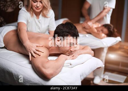 Handsome caucasian businessman and his beautiful wife treating themselves to a comforting back massage, a gentle relaxing massage at spa clinic. Stock Photo