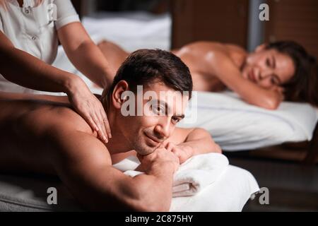 Everyday routine in massaging centre. Female and male therapists doing regenerating sports massage to caucasian sportive couple. Focus on woman. Stock Photo
