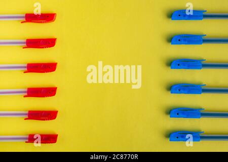 Blue and red ballpoint pens on a yellow background opposite each other on different sides. Flat lay, top view, space for text. Stock Photo