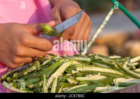 Young girl cutting okra lady finger with knife, preparing bhindi for cooking Stock Photo