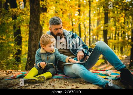 Homeschooling nature concept. Parent teach baby using laptop. Happy Father and son with spending time outdoor in the autumn park. Kid and his father Stock Photo