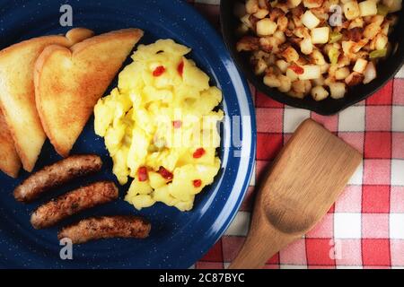 Country style scrambled eggs breakfast with peppers, sausage and toast on a rustic wooden restaurant table, with warm side light. Stock Photo