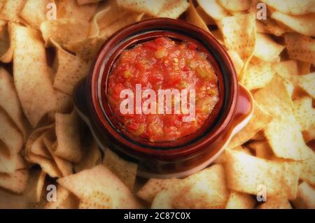 Flat lay still life image of a bowl filled with salsa surrounded by corn chips with warm side light. Stock Photo