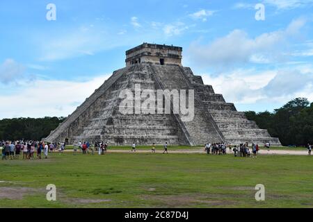 El Castillo at Chichen Itzá.  A step pyramid in the ancient Maya City in Mexico. Visitors gather on the grass around the main attraction. Stock Photo