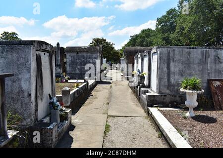 A view along a pathway of tombs and mausoleums in Lafayette Cemetery No 1 in the Garden District of New Orleans.  Weather worn tombs on a sunny day. Stock Photo