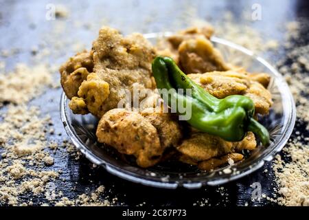 Famous Aloo pakora/ aloo bhajia in a glass plate with green chili and some chickpea flour spread on a surface.Shot of alu bhajiya on a transparent gla Stock Photo