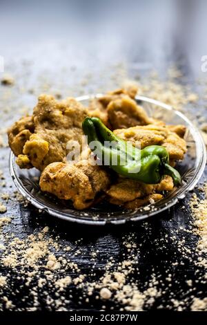 Famous Aloo pakora/ aloo bhajia in a glass plate with green chili and some chickpea flour spread on a surface.Shot of alu bhajiya on a transparent gla Stock Photo