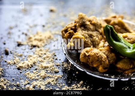 Famous Aloo pakora/ aloo bhajia in a glass plate with green chili and some chickpea flour spread on a surface.Shot of alu bhajiya on a transparent gla Stock Photo