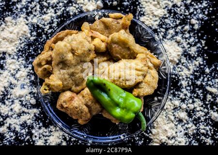 Famous Aloo pakora/ aloo bhajia in a glass plate with green chili and some chickpea flour spread on a surface.Shot of alu bhajiya on a transparent gla Stock Photo