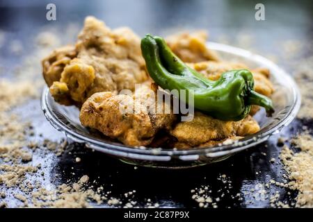 Famous Aloo pakora/ aloo bhajia in a glass plate with green chili and some chickpea flour spread on a surface.Shot of alu bhajiya on a transparent gla Stock Photo