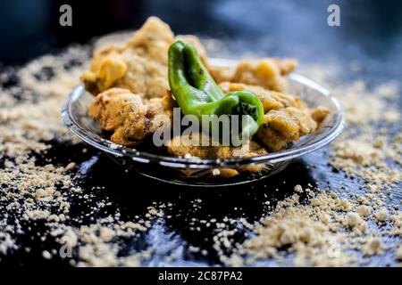 Famous Aloo pakora/ aloo bhajia in a glass plate with green chili and some chickpea flour spread on a surface.Shot of alu bhajiya on a transparent gla Stock Photo