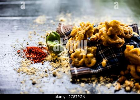 Famous kanda bhaji or kanda bhajiya or kanda pakora in a container on a black surface along with chickpea flour, spices, and all other ingredients for Stock Photo