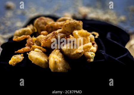 The famous shot of banana bhajia in a black colored container along with some raw banana and spices that are needed to make it. Stock Photo