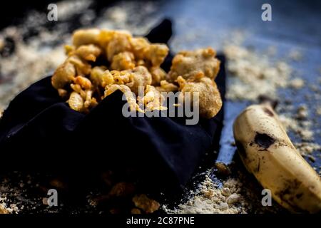 The famous shot of banana bhajia in a black colored container along with some raw banana and spices that are needed to make it. Stock Photo