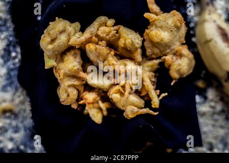 The famous shot of banana bhajia in a black colored container along with some raw banana and spices that are needed to make it. Stock Photo