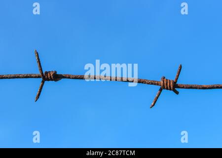 Fragment of old rusty barbed wire on blue sky background Stock Photo