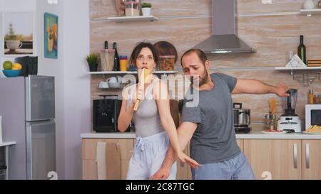 Carefree couple singing in the morning during breakfast. . Cheerful wife and husband laughing having fun funny enjoying life authentic married people positive happy relation Stock Photo