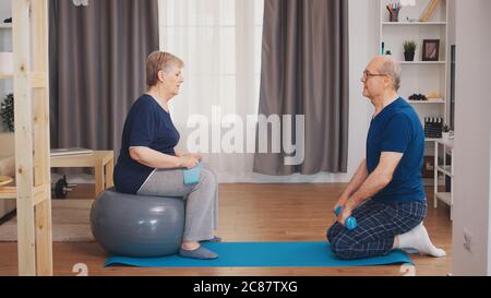 Senior couple exercising using yoga mat and stability ball. Old person healthy lifestyle exercise at home, workout and training, sport activity at home Stock Photo