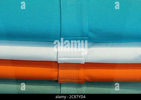 blue, white, orange and green colored shirts in a heap Stock Photo