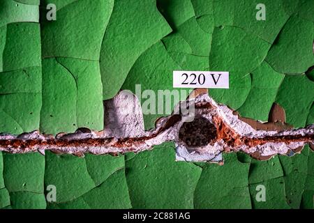 Old cracked wall with green peeling paint and empty rusty space for wiring with electricity sign, background Stock Photo