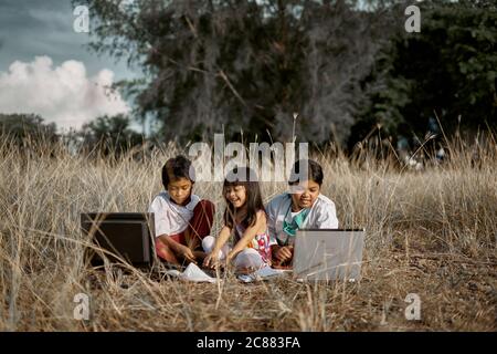 Three Cheerful children study using laptop at public park, Education New Normal concept Stock Photo