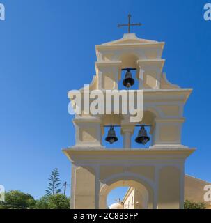 Traditional Greek Freestanding bell tower at church in Sidari, yellow white belfry with three bells and cross at Sidari, Corfu Greece, blue sky Stock Photo