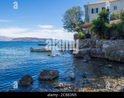 Pebble sea shore and The White House in Kalami, former residence of British authors Lawrence and Gerald Durrell and their family. Boat and pier at Stock Photo