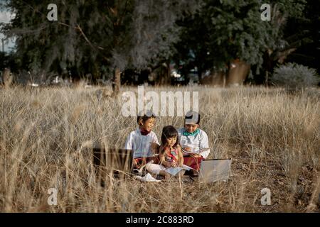 Three Cheerful children study using laptop at public park, Education New Normal concept Stock Photo