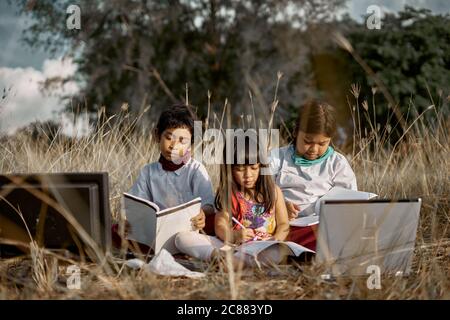 Three Cheerful children study using laptop at public park, Education New Normal concept Stock Photo