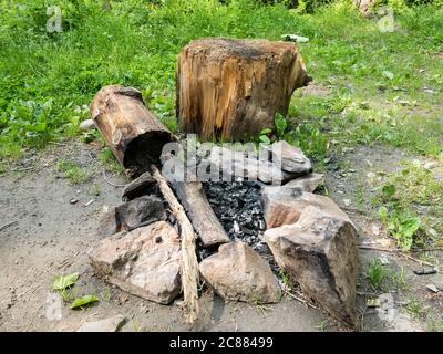 Stone camp fire pit with a log or stub for sitting down . Burnt wood in a camp fire Stock Photo