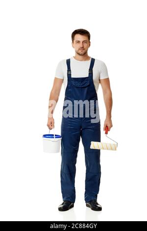 caucasian repairman in blue overalls holding paint roller and can with paint. builder or painter decorator isolated on white background Stock Photo