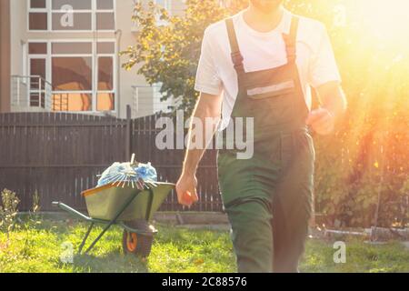 close-up of the gardener in green uniform in motion,in the background cart with bags and rakes. Stock Photo