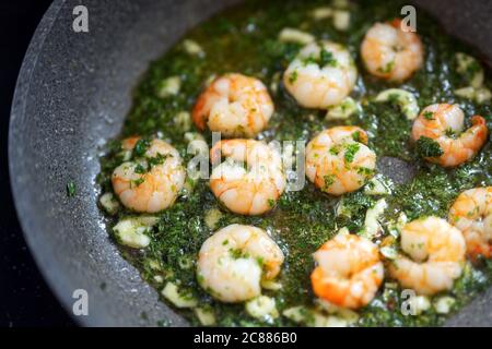 Shrimps with herbs and garlic oil are fried in a pan, cooking seafood concept, selected focus, very narrow depth of field