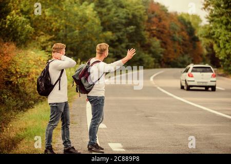 Meet New People. Looking for transport. twins walking along road. stop car with thumb up gesture. hitchhiking and stopping car with thumbs up gesture at countryside. On the road. Enjoying summer hike. Stock Photo