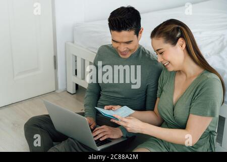 Cheerful Chinese man and woman smiling and using computer with home finances Stock Photo