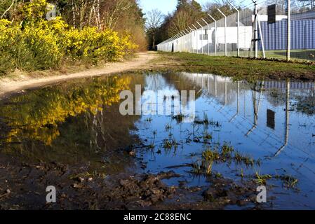 A barbed wire fence and blue sky reflected in a puddle on a clear day in early spring Stock Photo