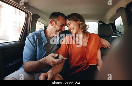 Happy couple smiling in the backseat of a car. Couple in love traveling by a cab. Stock Photo