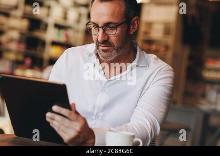 businessman working on his digital tablet sitting at a coffee shop. Man using his table pc at cafe. Stock Photo