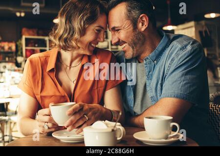 Loving couple sitting at cafe touching foreheads and smiling. Beautiful couple in love having a coffee date. Stock Photo