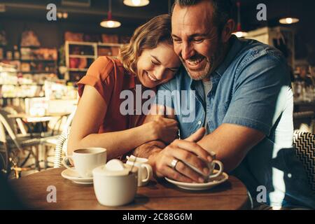 Woman smiling and putting her head on shoulder of man while sitting at a  coffee shop. Loving couple on a coffee date together. Stock Photo