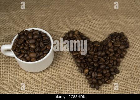 Heart shape made from coffee beans and cup of coffee on hessian spelling I love coffee Stock Photo
