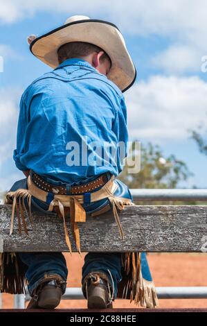 A young cowboy in full regalia sits on the rodeo rails watching the action before his own event at Mt Garnet, Queensland, Australia. Stock Photo